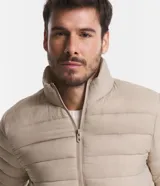 Campera puffer ultraligera color beige, con cuello alto, cierre por cremallera y bolsillos con cremallera. Incluye bolso de almacenamiento.