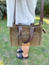 Cartera bandolera de cuero color verde oliva, con forro de tela, bolsillo delantero con cierre y bolsillo interno. Tiene correa larga regulable y manijas cortas.