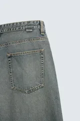 Pantalón de jean gris oscuro, corte amplio, con cinco bolsillos, efecto lavado y cierre frontal con cremallera y botón.