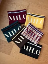 Clutch o neceser negro de neopreno con cierre de cremallera blanco y logo grande en blanco con tipografía serif.