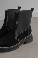 Bota corta negra de gamuza y neopreno, con elástico lateral y costuras blancas. Tiene suela track y tirador trasero.
