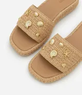 Sandalia plana flatform color beige, con textura trenzada y apliques de colgantes metálicos con motivos marinos.