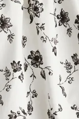 Vestido corto blanco con estampado floral negro, breteles finos, escote corazón y falda con vuelo.