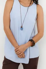 Musculosa color crudo con cuello redondo y ribete marrón en cuello, sisas y ruedo. Diseño cruzado en el frente y aberturas laterales.