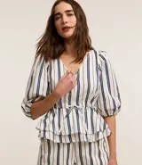 Blusa de sarga a rayas verticales blancas y azules, con cuello en V, mangas cortas abullonadas, lazo en la cintura y volado en el bajo.