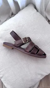 Sandalias de cuero color marrón con tiras entrecruzadas y hebilla metálica.