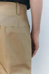 Pantalón color beige de corte ancho, con tiro medio, trabillas en la cintura y raya planchada.