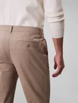 Pantalón chino de corte slim color beige, confeccionado en algodón y elastano. Presenta cierre con cremallera y botón, diseño clásico de cuatro bolsillos y logo de Calvin Klein bordado en la parte posterior.