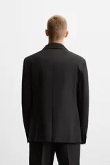 Blazer negro de lana con cuello de solapa de muesca, corte recto, manga larga con puños abotonados, bolsillos de vivo en el pecho y de solapa en la cadera, abertura en la parte posterior y cierre frontal con botones. Colección Origins.