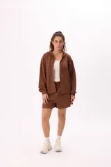 Conjunto deportivo color marrón, compuesto por un buzo con capucha, cierre frontal, bolsillos y terminaciones metálicas, y un short con cintura elástica ajustable con cordón.