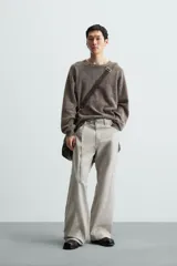 Pantalón de algodón color beige claro, estilo relaxed fit, con cintura ajustable mediante cinturón de tela a juego. Presenta cinco bolsillos, bolsillos laterales de vivo y costuras laterales giradas hacia adelante.