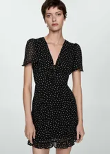 Vestido corto negro con estampado de lunares blancos, escote en V con lazo, mangas cortas y falda con volantes.