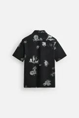 Camisa negra con estampado floral en tonos grises, de manga corta y cuello bowling.