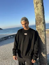 Buzo negro oversize con cuello redondo y logo ovalado bordado en el pecho.