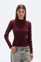Sweater de punto color borgoña, con cuello alto y botones metálicos decorativos en hombros y mangas.