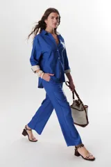 Camisa verde militar de manga larga con puños color crema, cuello clásico y cierre frontal con botones. Tiene un bolsillo en el pecho con bordado de una palmera color crema.