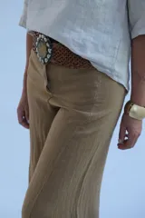Pantalón camel de corte palazzo, tiro alto y confeccionado en lino. Presenta cintura con trabillas y cinturón trenzado con hebilla circular.