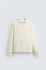 Sudadera color crema de corte regular, con cuello alto y cierre frontal de cremallera metálica.