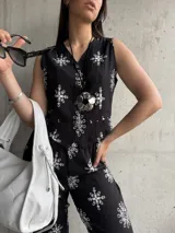 Chaleco negro con estampado de flores blancas, sin mangas, con cuello en V y cierre frontal con botones.