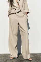 Pantalón color beige de lino, de tiro alto con cintura elástica, bolsillos laterales ocultos en costura y pernera ancha.