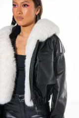 Campera corta negra de cuero sintético con capucha y cuello de piel sintética blanca desmontable, cierre frontal con cremallera, bolsillos delanteros con solapa y puños ajustables con botones a presión.