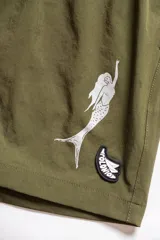 Short de baño verde oliva con cintura elástica y cordón ajustable. Presenta bordados de sirenas en las piernas y un parche con logo.