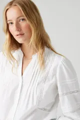 Camisa blanca de mangas largas con detalles de encaje en el frente y en las mangas.