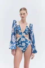 Body de lycra azul con estampado floral blanco, escote en V, mangas largas abullonadas con hombreras y puños elásticos. Detalles de bordado en cordón y pedrería en escote y cintura.