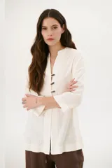 Sobrecamisa beige de corte recto, cuello mao y mangas 3/4. Presenta cierre frontal con botones de madera y bolsillos laterales.