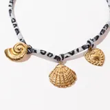 Collar corto con cordón estampado animal print en tonos grises y dijes colgantes dorados en forma de corazón, caracol y concha.