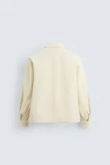 Sobrecamisa color crudo de corte regular fit, confeccionada en tejido con mezcla de viscosa. Tiene cuello solapa, manga larga con puños abotonados, bolsillo de parche en el pecho, bajo ajustable con cordones y cierre frontal con botones.