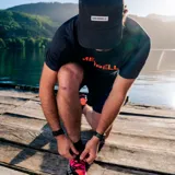 Remera deportiva naranja de poliéster y spandex, con logo Merrell estampado en el pecho.