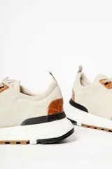 Zapatillas deportivas color beige con detalles en cuero marrón y suela de goma blanca y marrón.
