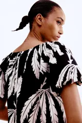Vestido corto evasé de algodón con estampado de hojas color blanco sobre fondo negro. Tiene mangas globo cortas de diseño raglán y escote redondo con cordón para ajustar.