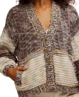 Cárdigan grueso de punto con diseño patchwork en tonos marrones, beige y toques de color pastel. Presenta cuello V, botones frontales y bolsillos amplios en la parte delantera. Las mangas son largas y abullonadas.