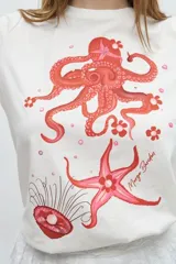 Remera blanca de algodón con estampado de pulpo, estrella de mar y medusa en tonos rosados.