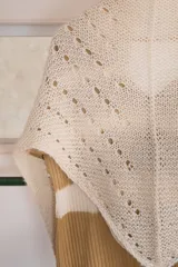 Chal triangular tejido a mano en lana de alpaca natural color crudo, con diseño calado y terminación con borlas.