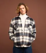 Campera trucker masculina de franela a cuadros en tonos blanco, negro y gris, con cuello inglés, abotonado delantero, bolsillos con solapa en el pecho y bolsillos laterales. Interior forrado en sherpa.