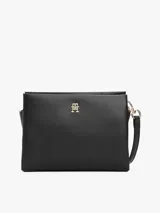 Cartera bandolera negra con textura granulada, correa ajustable y logo metálico dorado de Tommy Hilfiger en el frente.