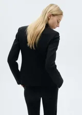 Chaqueta negra con cuello de pico con solapa y cierre de botón en la parte delantera. Tiene manga larga con puños abotonados, diseño recto, estilo traje y dos bolsillos de solapa en la parte delantera.