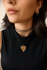 Collar con tiento encerado negro y dije dorado con forma de corazón texturizado.
