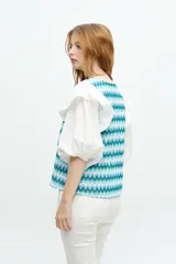 Blusa blanca con mangas abullonadas y volados en las sisas. El cuerpo de la blusa es de tela bordada con pequeños orificios.