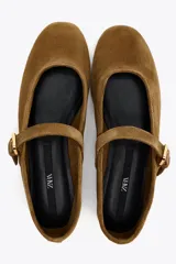 Zapato plano tipo bailarina en serraje color marrón. Escote redondo y cierre mediante hebilla en el empeine.