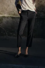 Pantalón negro tobillero de tiro medio con cintura elástica en la espalda, bolsillos delanteros y falsos bolsillos de vivo en la espalda. Bajo con aberturas laterales. Cierre frontal con cremallera, botón interior y gancho.