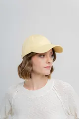Gorra de béisbol color amarillo pastel, con visera curva y logo de Peach bordado en el frente. Ajustable en la parte trasera.