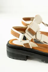 Sandalias con plataforma color marrón, con tiras de cuero color blanco y marrón con hebillas metálicas.