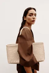Bolso shopper alargado color beige con diseño trenzado, doble asa de hombro y cierre con botón imantado. Incluye bolsa interior con cierre fruncido.