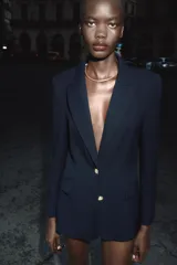 Blazer negra entallada con cuello solapa, manga larga con hombreras, bolsillos delanteros con solapa y cierre frontal con botones dorados.