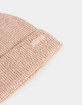 Gorro de lana tejido color rosa viejo, con pompón de piel sintética en la parte superior y etiqueta de goma con la inscripción "Joyful Spirit" en el borde.