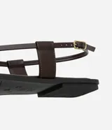 Sandalia plana color marrón con punta cuadrada, tiras finas con flor central y strass, y cierre de tira fina con hebilla cuadrada.